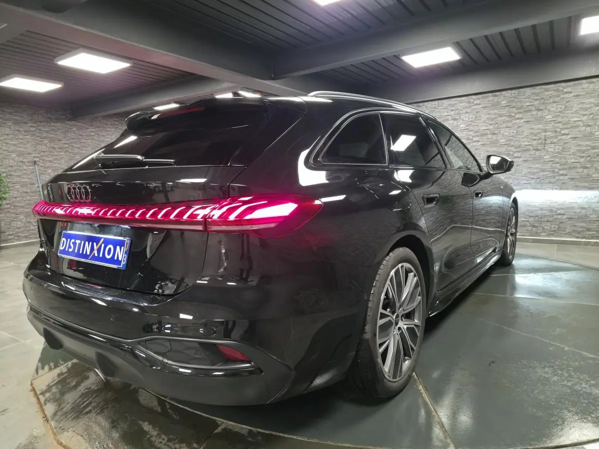 Audi A5 Avant noir vue 3/4 arrière droit, feux arrière LED allumés et jantes 19 pouces gris graphite brillantes.