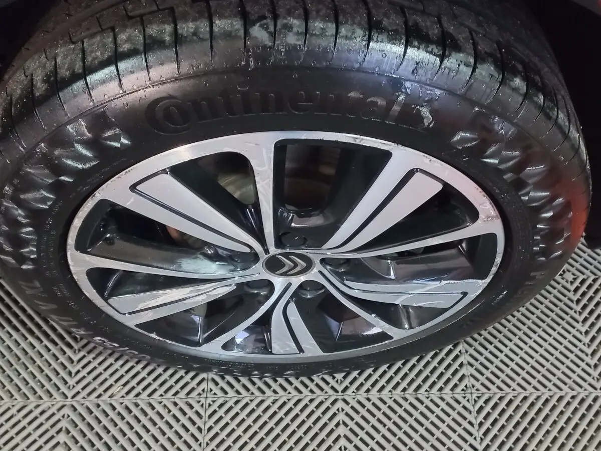 Gros plan sur la jante alliage noire et argentée avec logo Citroën, pneu Continental humide, sol en grille plastique.