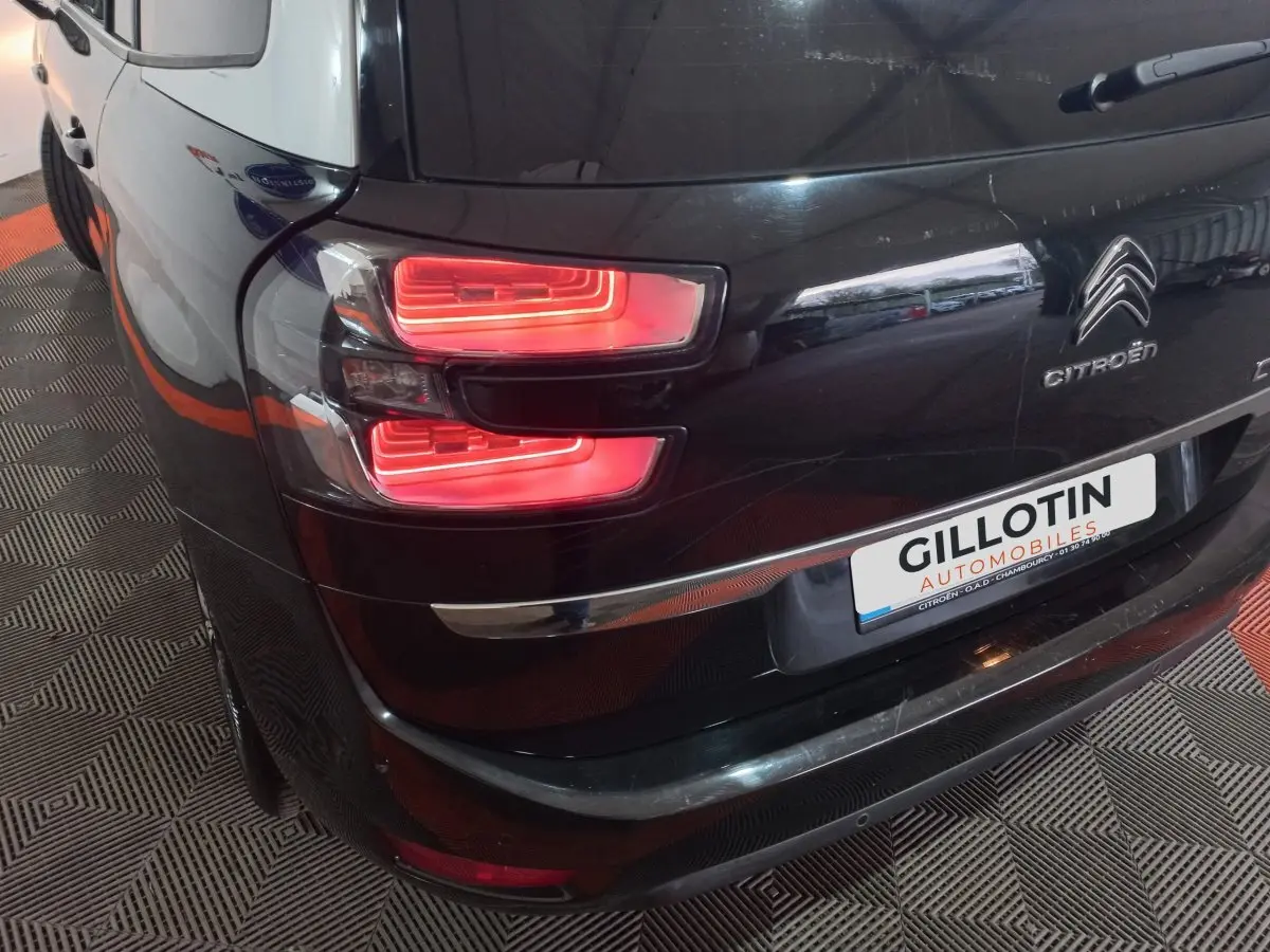 Vue arrière côté gauche d'un Citroën Grand C4 Spacetourer noir avec feux arrière allumés et logo visible.