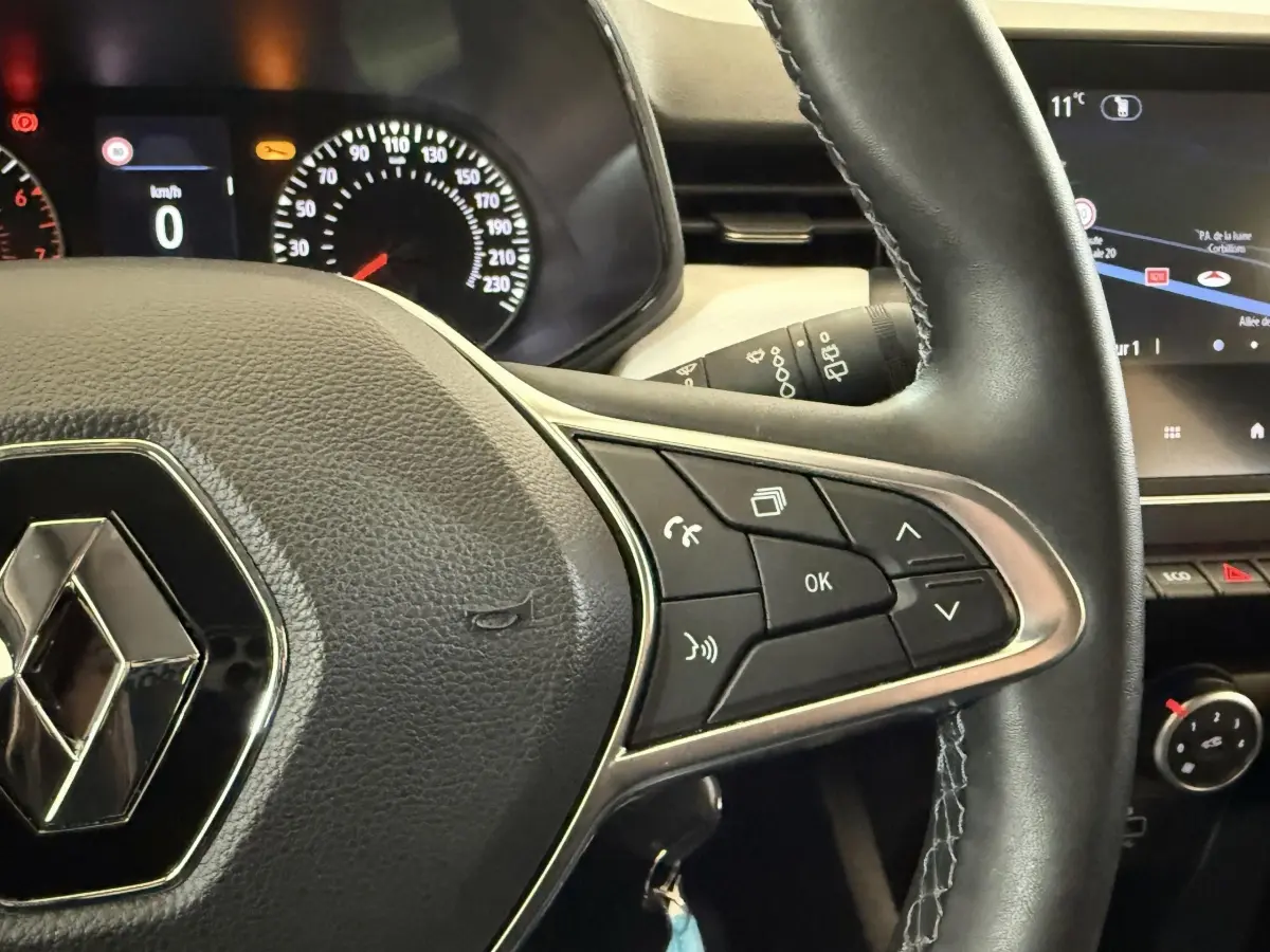 Gros plan sur le volant cuir synthétique noir de la Renault Clio Business, avec commandes multifonctions et tableau de bord partiel.