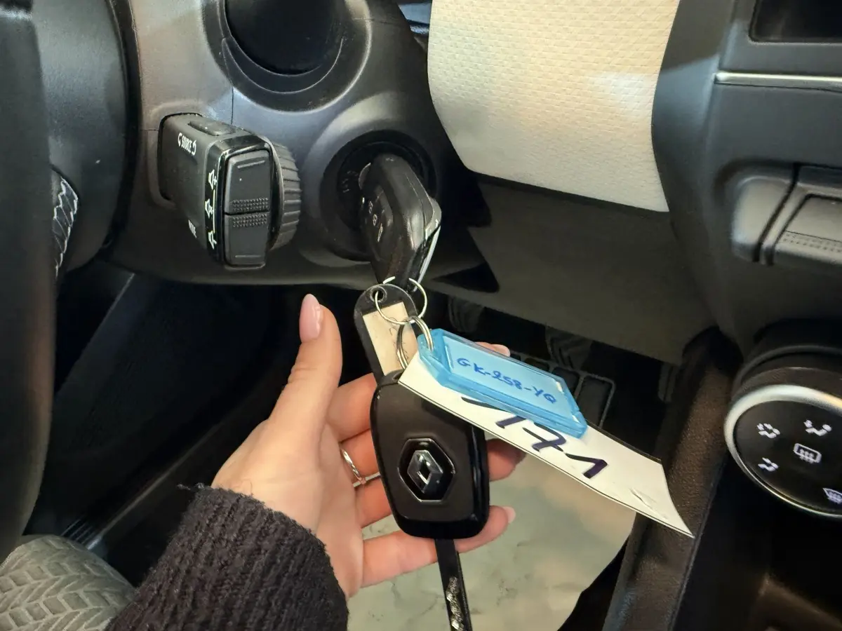 Main tenant la clé Renault insérée dans le contacteur, vue intérieure côté conducteur du tableau de bord noir et beige.