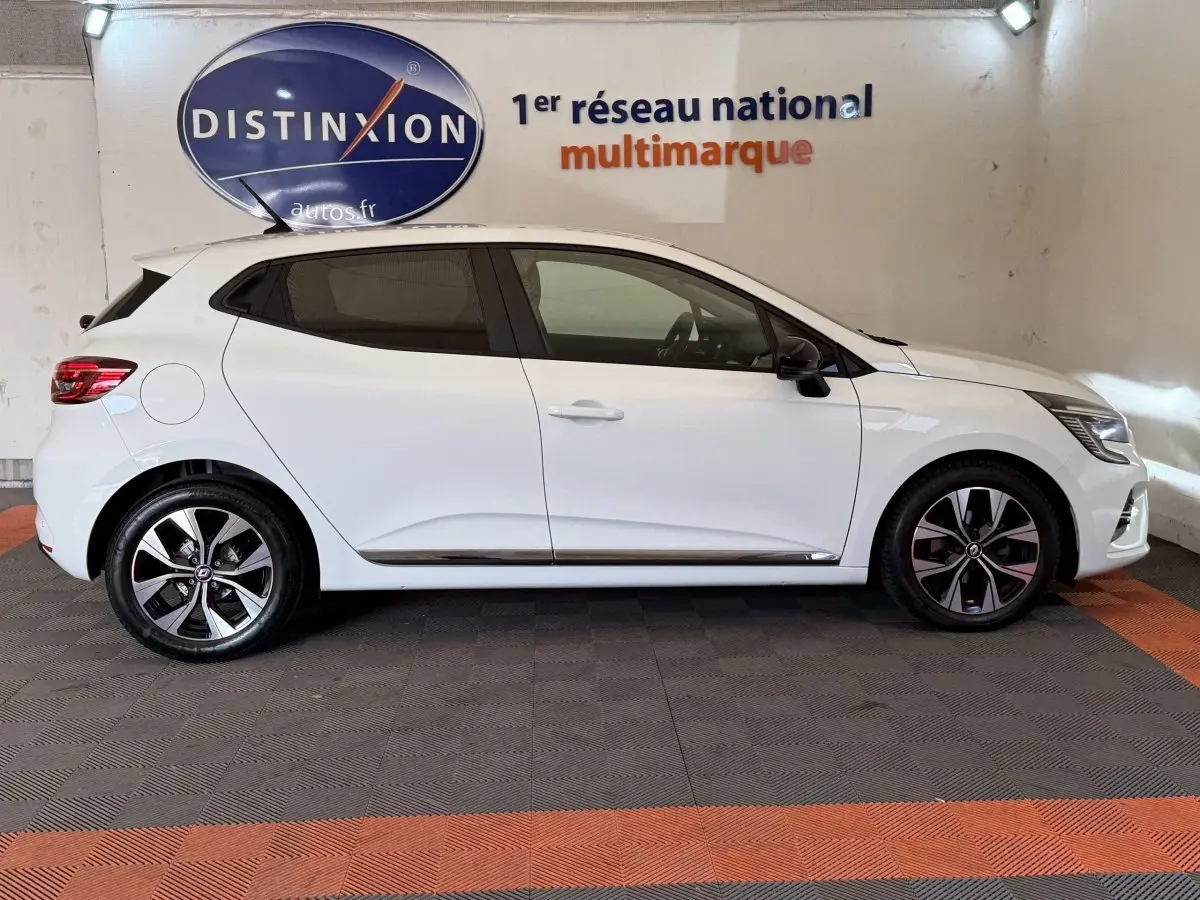 Profil droit d'une Renault Clio Business TCe 100 GPL blanche, avec jantes alliage et vitres teintées, en intérieur showroom.