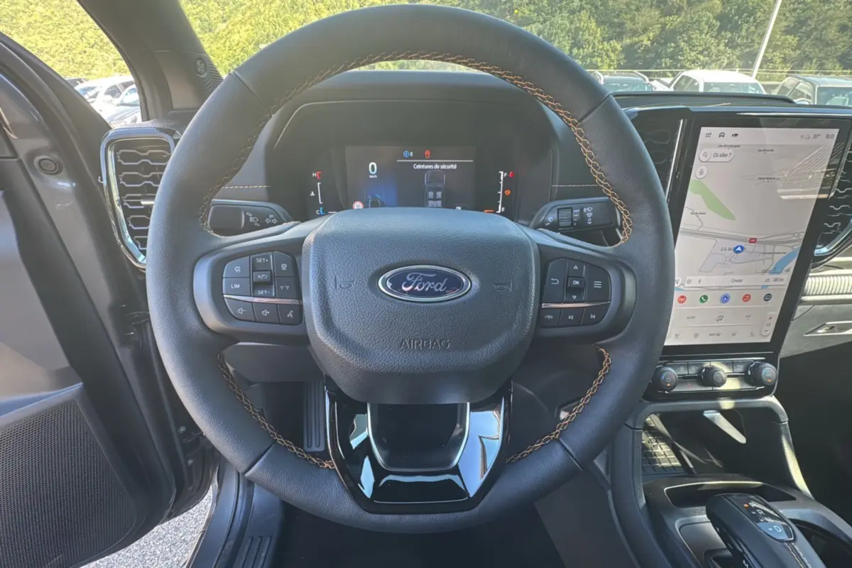 Vue intérieure centrée sur le volant cuir noir avec surpiqûres marron du Ford Ranger 2025, écran tactile et tableau de bord numériques visibles.
