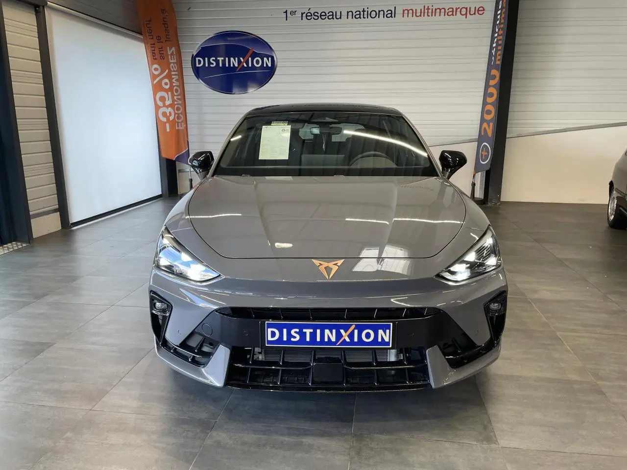 Vue avant d'une CUPRA Leon gris Graphène avec logo cuivré et phares LED allumés en showroom.