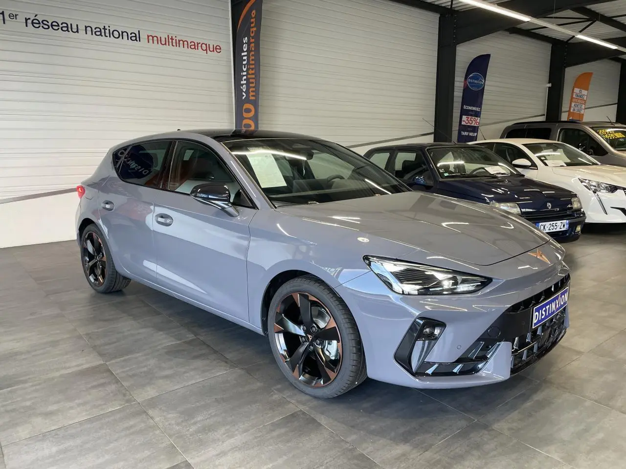 Vue 3/4 avant d'une CUPRA Leon gris Graphène avec jantes alliage noires et cuivrées en showroom.