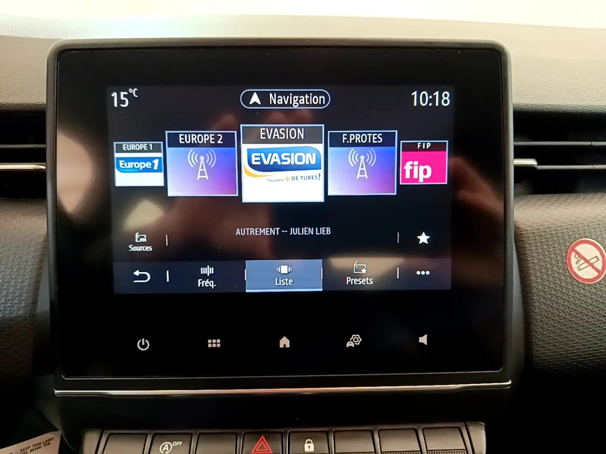 Écran tactile central de la Renault Clio Business blanche, affichant les radios et la navigation, vue de face.