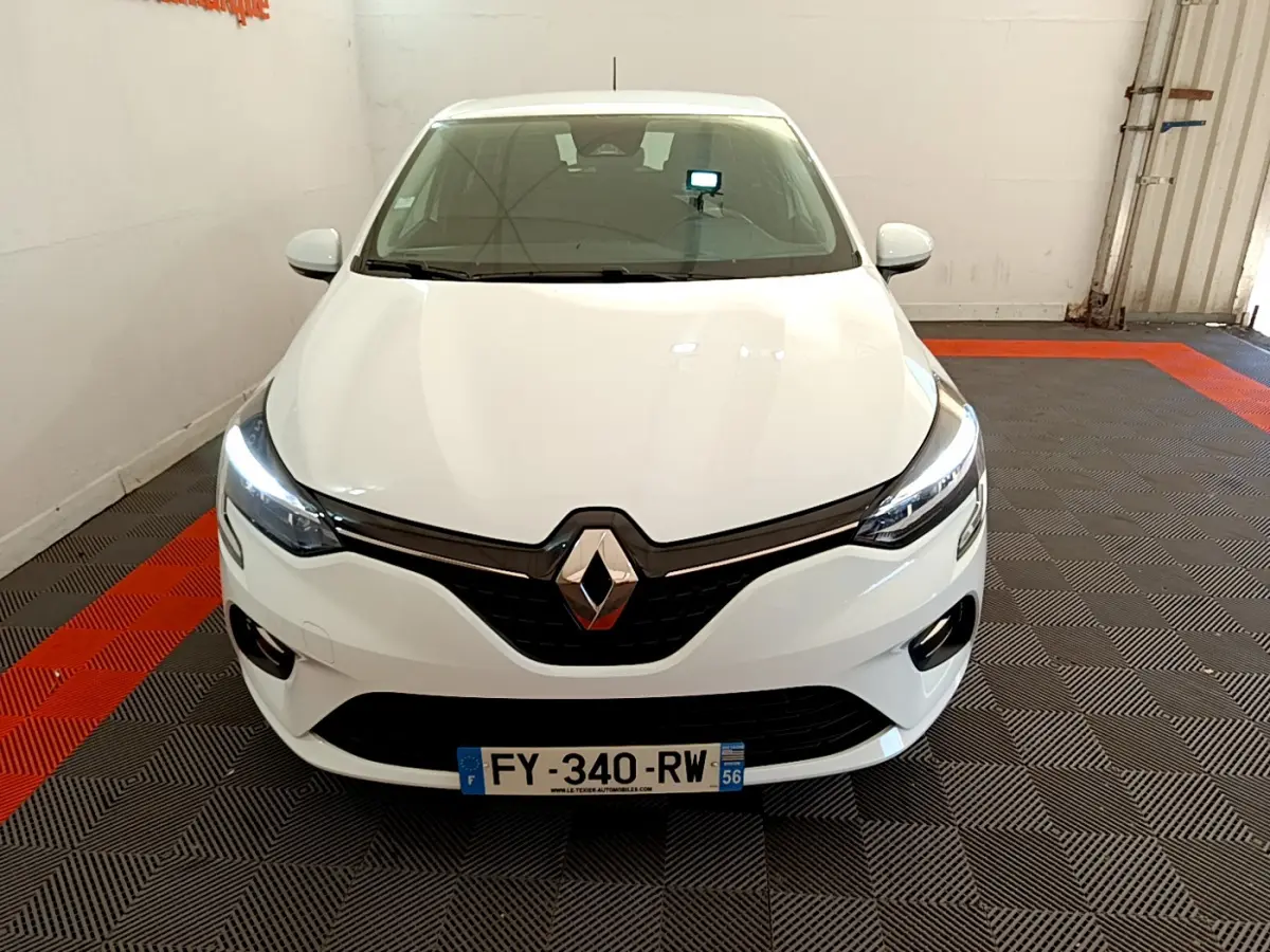 Vue de face d'une Renault Clio Business blanche 2021 avec phares LED allumés dans un garage.