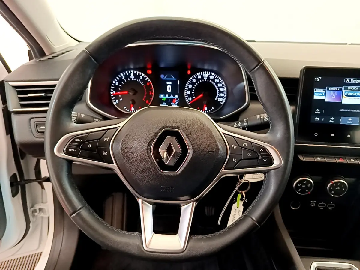 Vue centrée sur le volant cuir noir de la Renault Clio Business blanche, avec tableau de bord et écran tactile visible à droite.