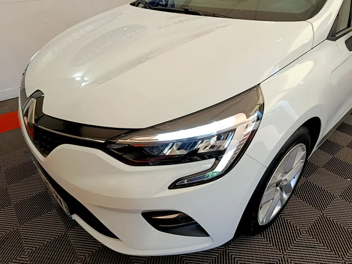 Vue 3/4 avant droit d'une Renault Clio Business blanche mettant en valeur ses phares LED et sa calandre noire brillante.