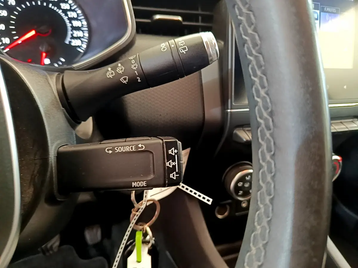 Gros plan sur le volant cuir et commandes au volant d'une Renault Clio Business blanche, tableau de bord partiellement visible.