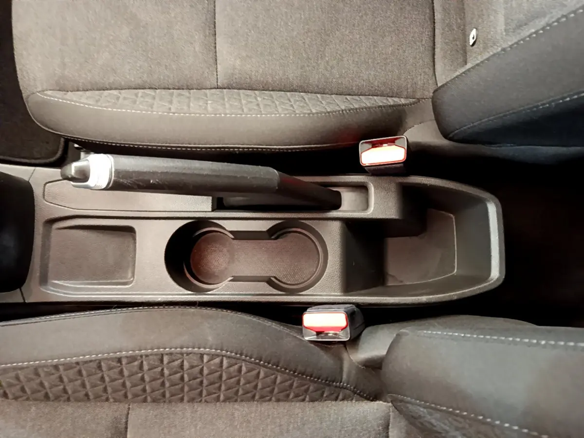 Vue plongeante sur la console centrale noire de la Renault Clio Business blanche avec frein à main et porte-gobelets.