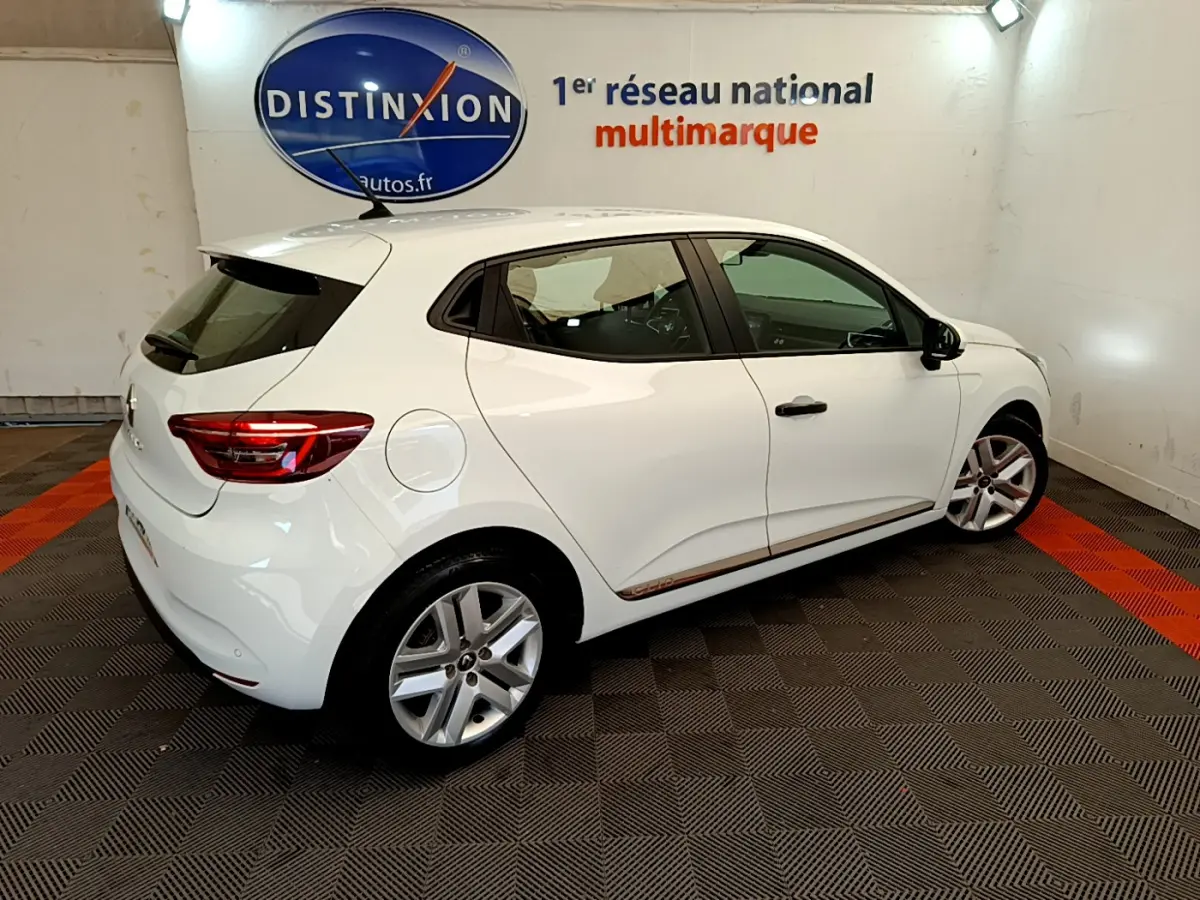 Vue 3/4 arrière droite d'une Renault Clio Business blanche, avec jantes alliage et logo Distinxion en arrière-plan.