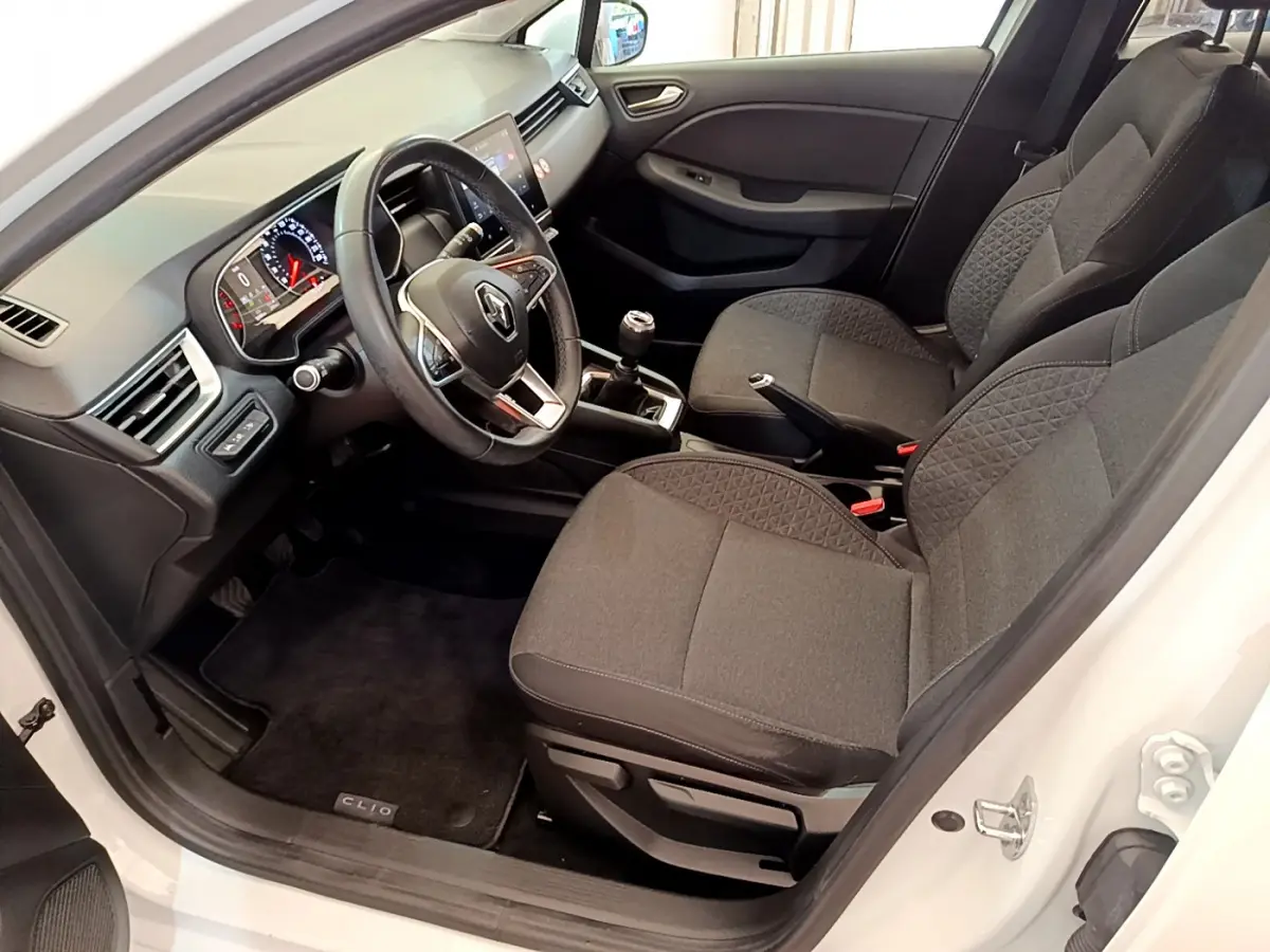 Intérieur avant droit de la Renault Clio Business blanche, sièges gris, volant cuir et tableau de bord avec écran tactile.