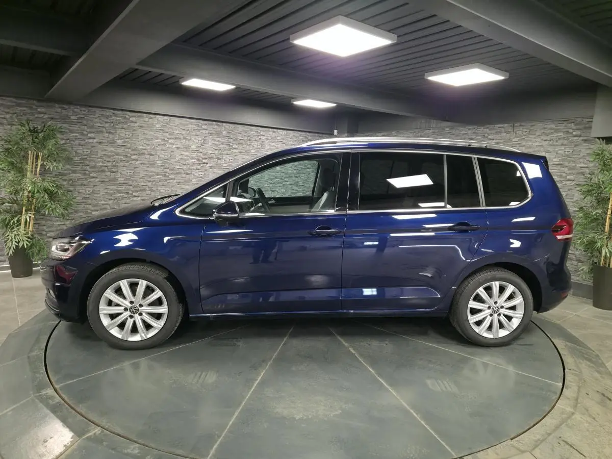 Profil côté gauche d'un Volkswagen Touran bleu métallisé 2024 dans un showroom avec jantes alliage 17 pouces.