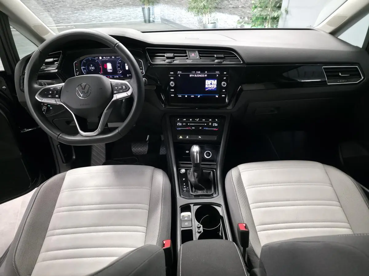 Vue intérieure avant du Volkswagen Touran 2024, tableau de bord noir avec sièges gris clair et console centrale équipée.