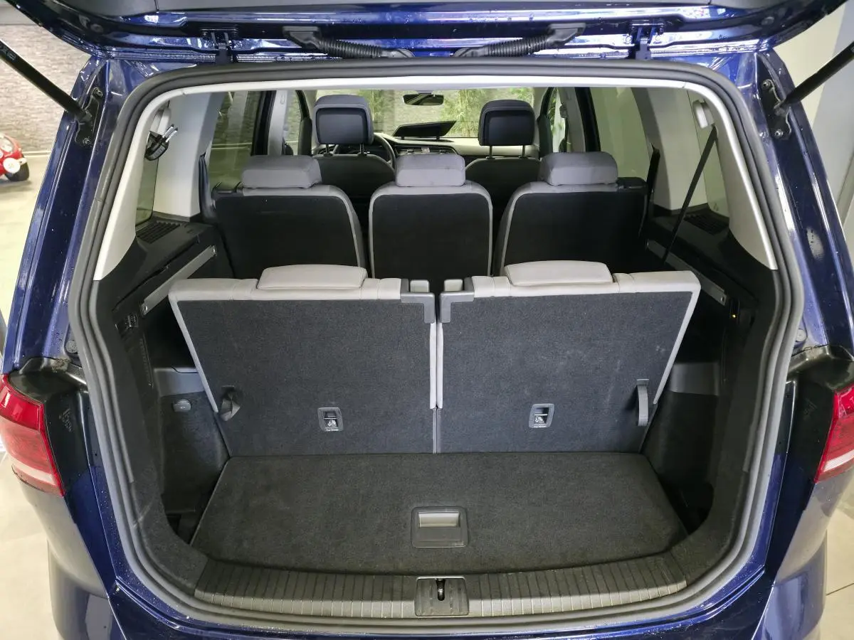 Vue arrière du coffre ouvert d'un Volkswagen Touran bleu 2024 montrant les sièges arrière rabattus et l'intérieur spacieux.