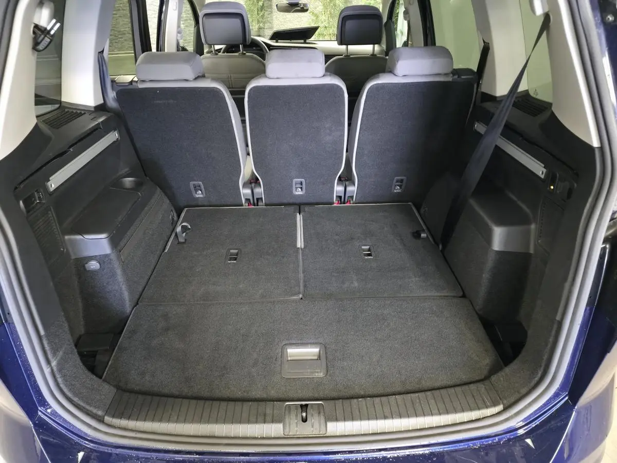 Coffre ouvert du Volkswagen Touran bleu 2024, vue arrière montrant les sièges arrière relevés et plancher de coffre plat.