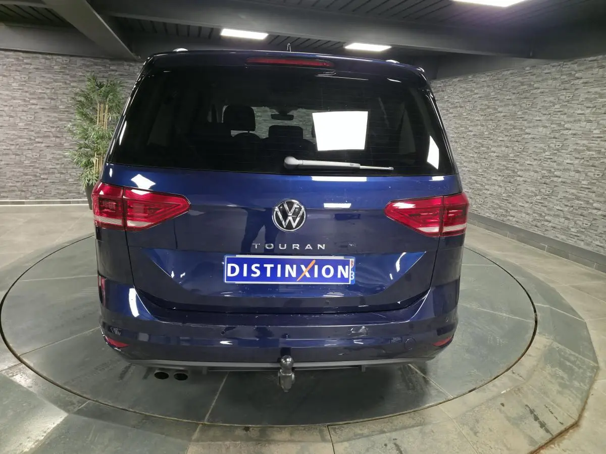 Vue arrière d'un Volkswagen Touran bleu 2024 avec crochet d'attelage escamotable et feux arrière LED.