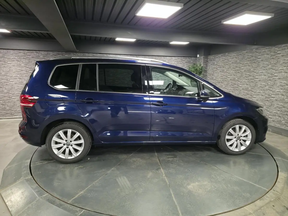 Profil côté gauche d'un Volkswagen Touran bleu métallisé 2024 dans un showroom avec jantes alliage 17 pouces.