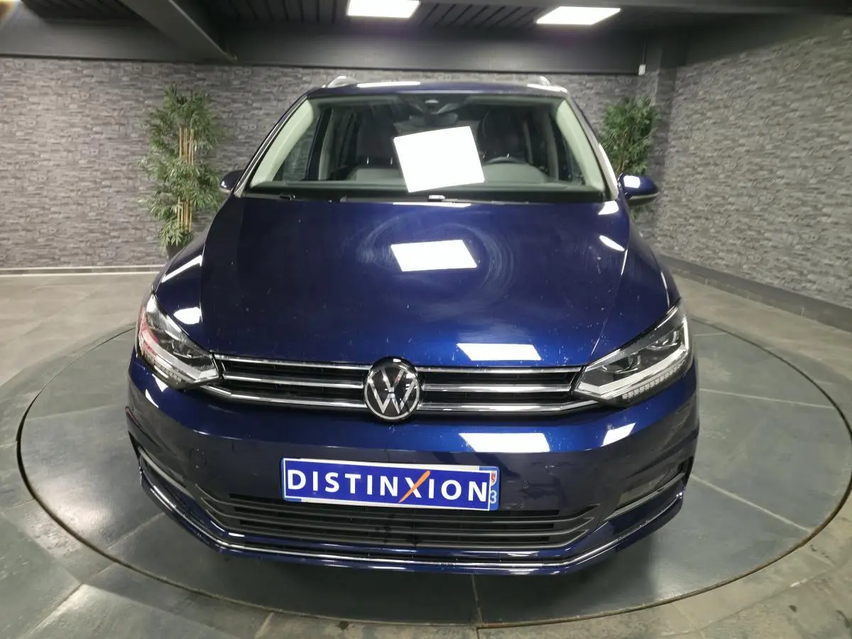 Vue frontale d'un Volkswagen Touran bleu métallisé 2024 avec calandre chromée et plaque Distinxion.