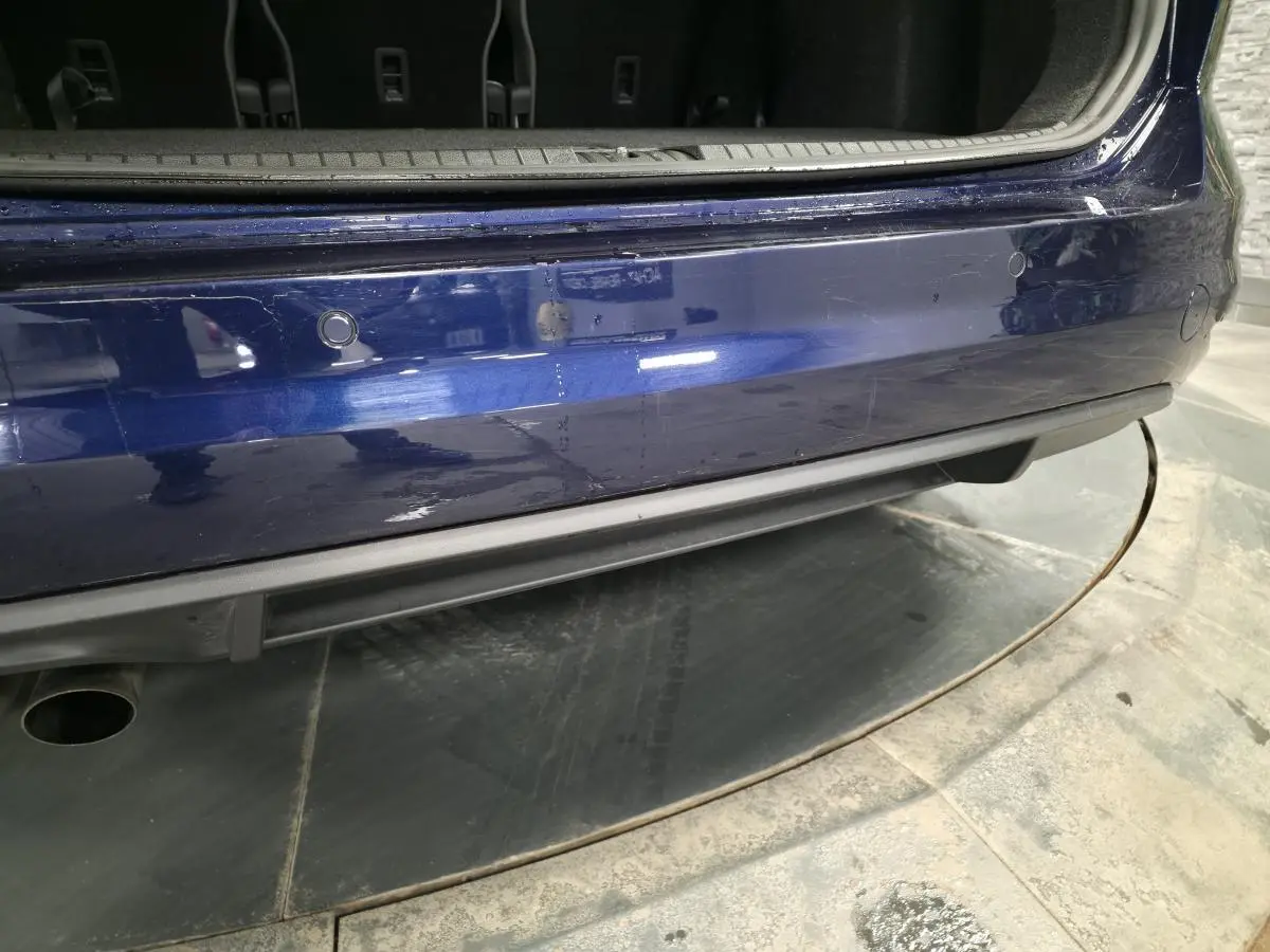 Gros plan sur le pare-chocs arrière bleu métallisé du Volkswagen Touran 2024 avec capteurs de recul visibles.