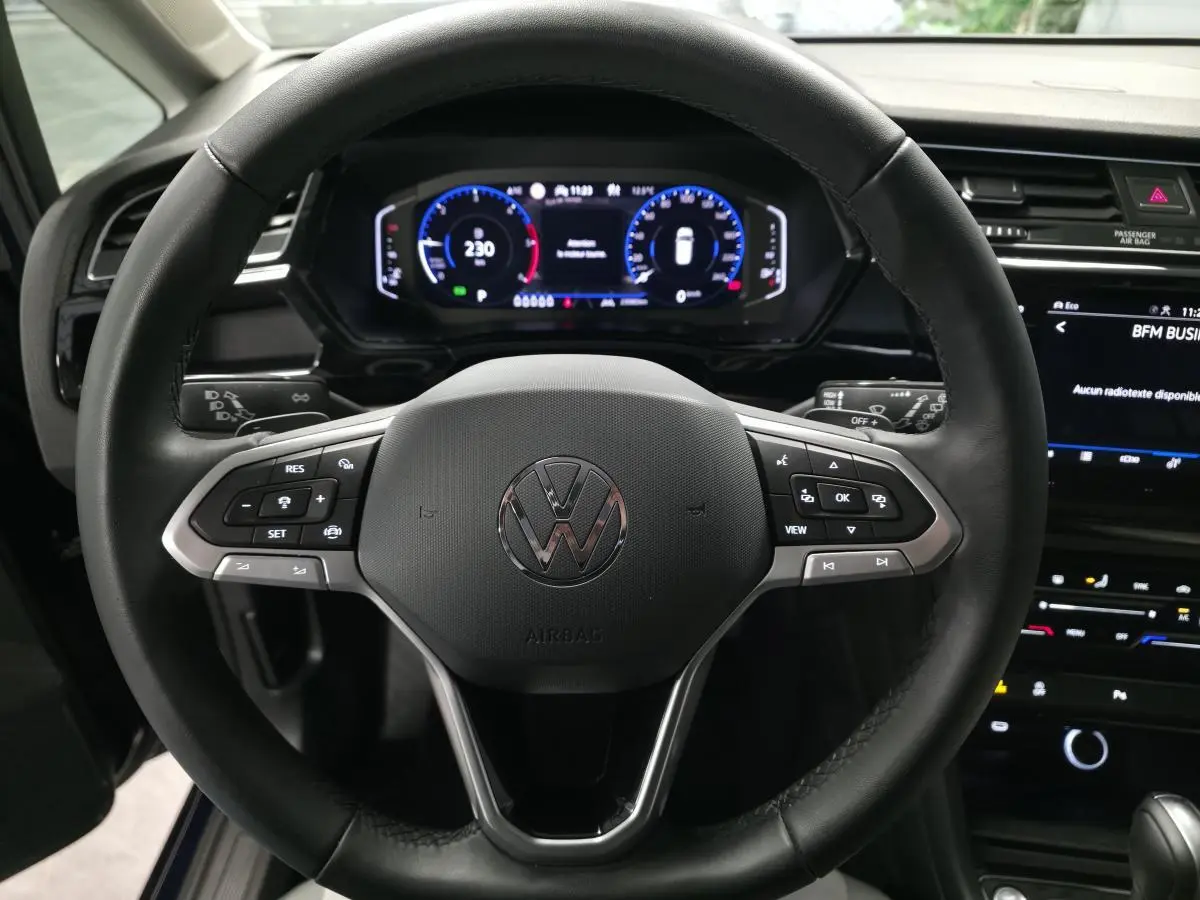 Gros plan sur le volant cuir multifonction noir du Volkswagen Touran 2024 avec tableau de bord numérique et écran tactile.