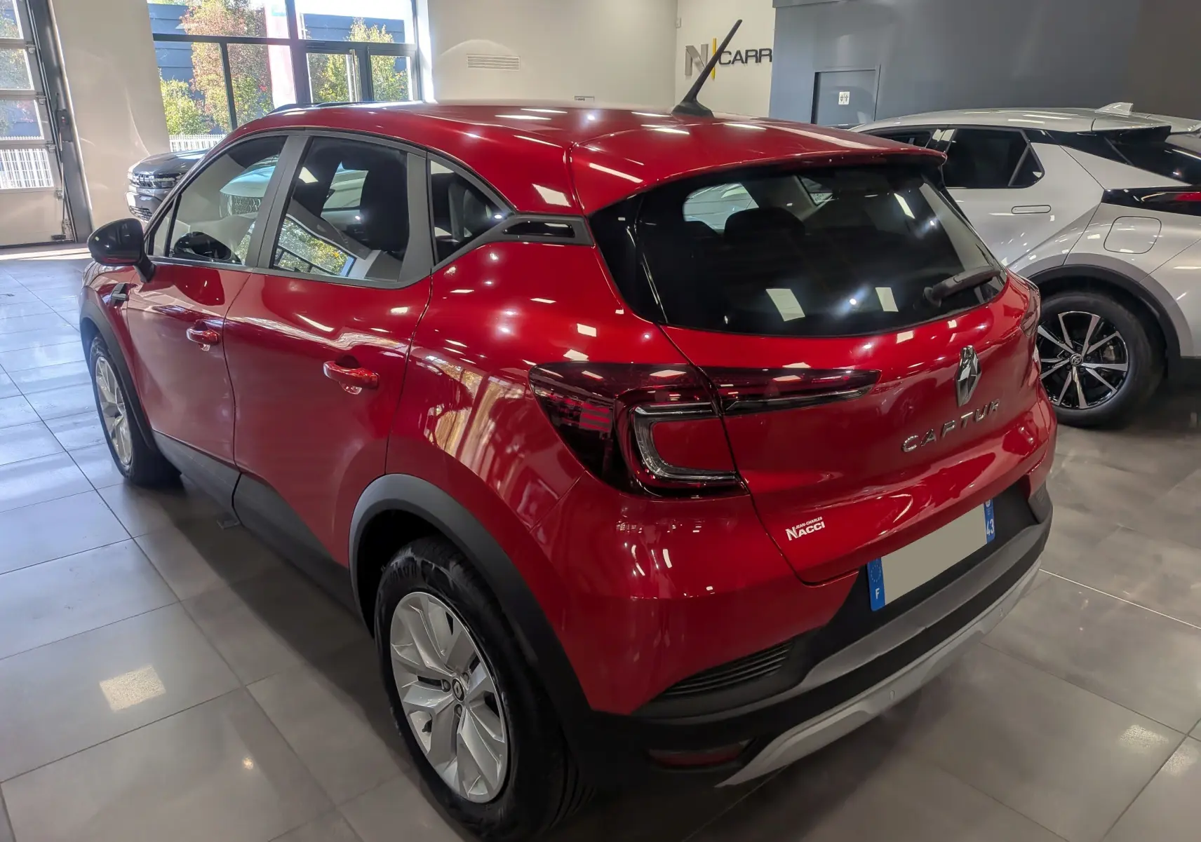 Vue 3/4 arrière gauche d'un Renault Captur Rouge Flamme 2023 en showroom avec feux arrière LED distinctifs.