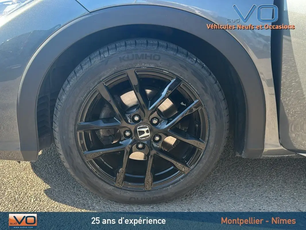 Gros plan sur la jante alliage noire côté gauche d'une Honda Civic gris 2015 avec logo Honda au centre.