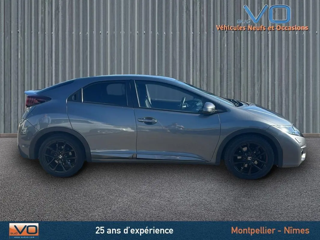 Profil côté gauche d'une Honda Civic gris 2015 avec jantes alliage noires et vitres surteintées sur fond industriel.