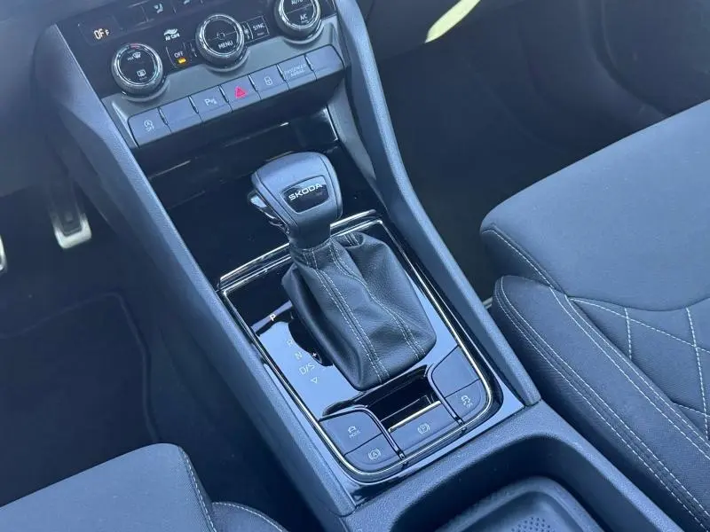 Vue rapprochée de la console centrale noire avec levier de vitesses automatique marqué SKODA et sièges tissu noir du Karoq 2025.