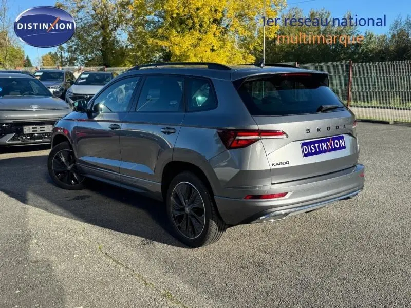 Vue 3/4 arrière droite d'un Skoda Karoq gris perle avec jantes alu et barres de toit noires.