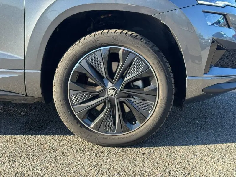 Gros plan sur la roue avant gauche d’un Skoda Karoq gris perle avec jante alu noire au design moderne.