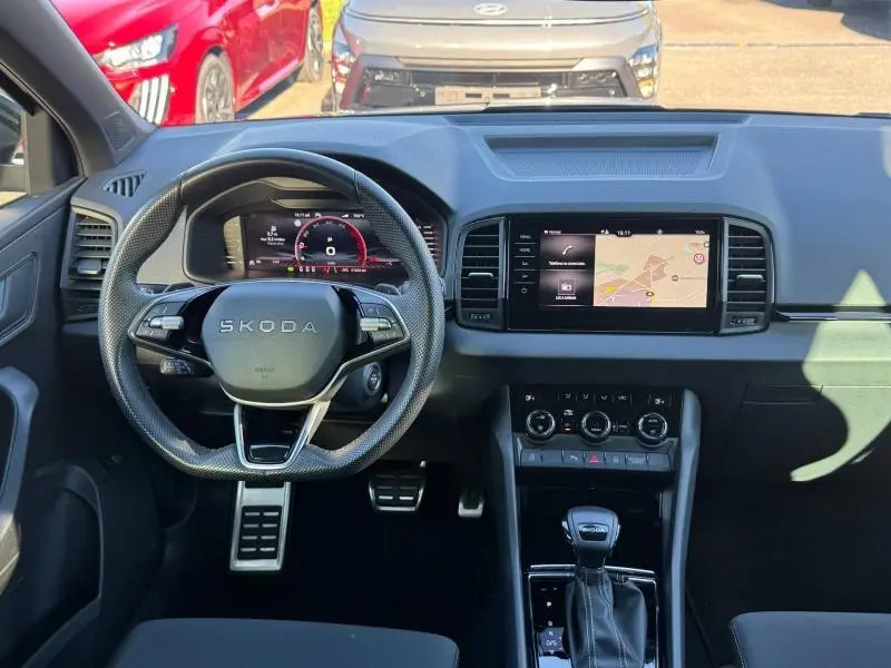 Vue intérieure frontale du tableau de bord et volant cuir noir du Skoda Karoq gris avec écran tactile GPS et palettes au volant.