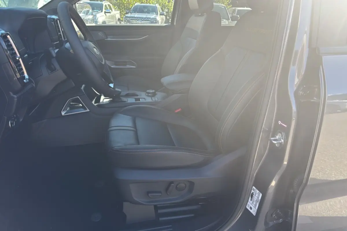 Vue intérieure côté conducteur du Ford Ranger gris carbone 2025, sièges cuir noirs avec surpiqûres orange et logo Wildtrak brodé.