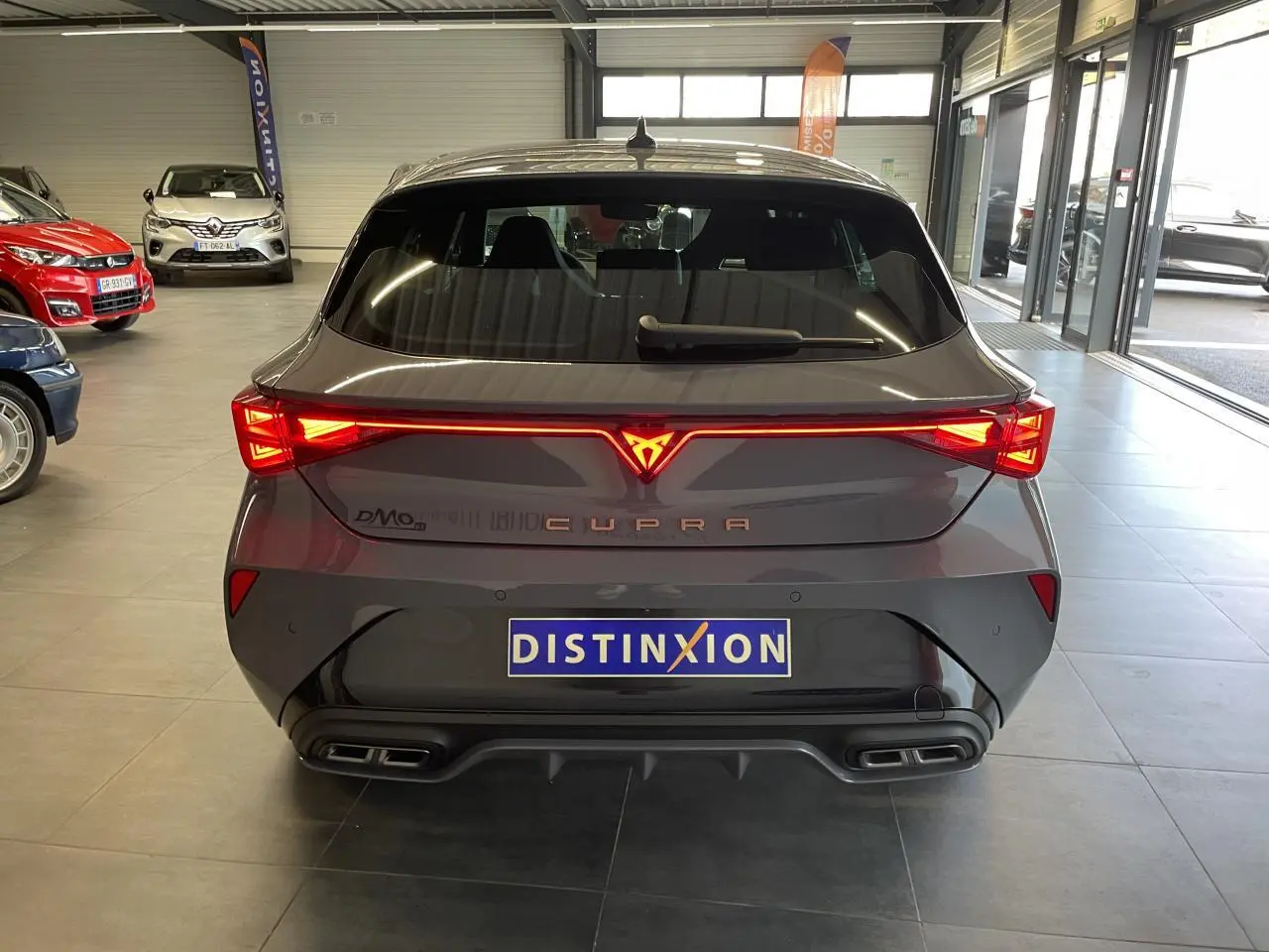 Vue arrière d'une CUPRA Leon gris Graphène avec feux arrière en bandeau lumineux et double sortie d'échappement noire.