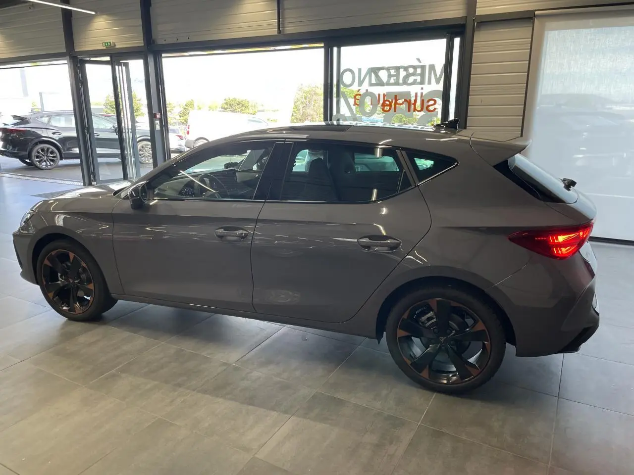 Vue latérale droite d'une CUPRA Leon 2.0 TDI gris Graphène avec jantes alliage 18'' cuivrées en showroom.