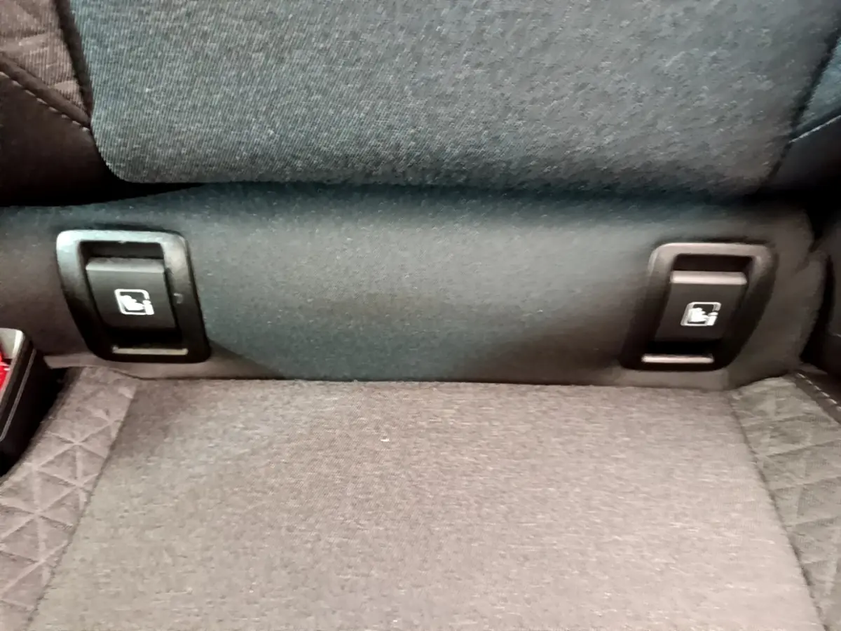 Gros plan sur les commandes de rabattement des sièges arrière en tissu gris de la Renault Clio Business blanche.