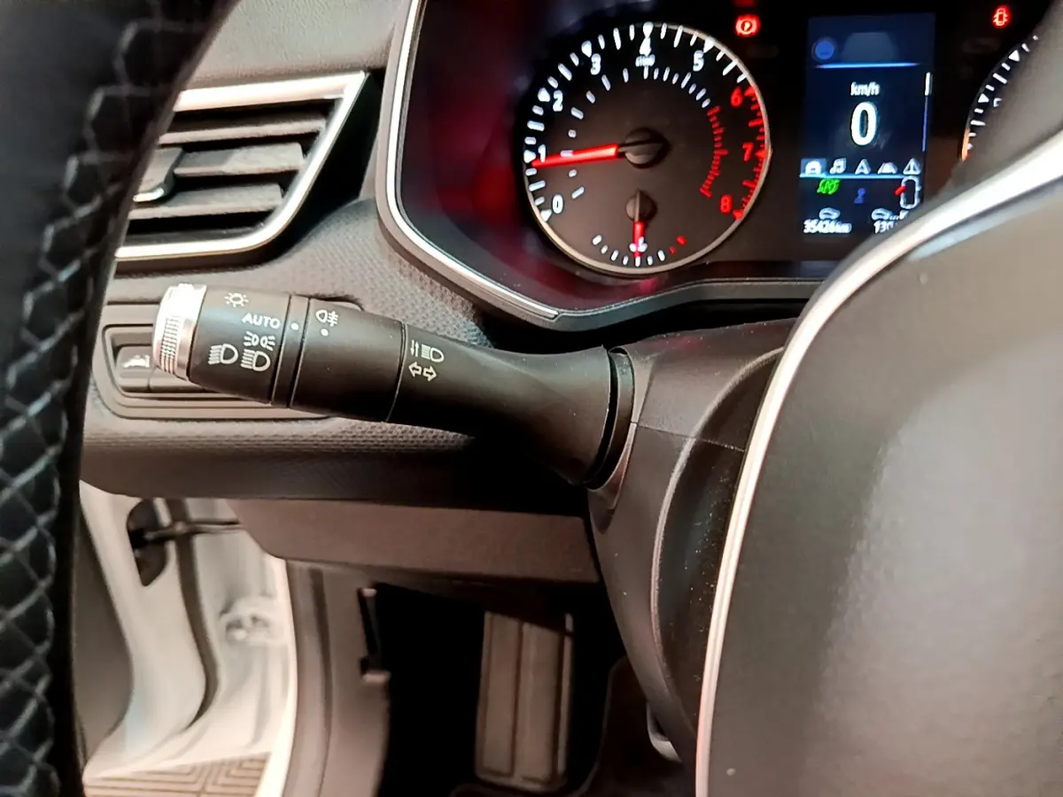 Gros plan sur le commodo gauche et le tableau de bord numérique de la Renault Clio Business blanche, affichant 0 km/h.