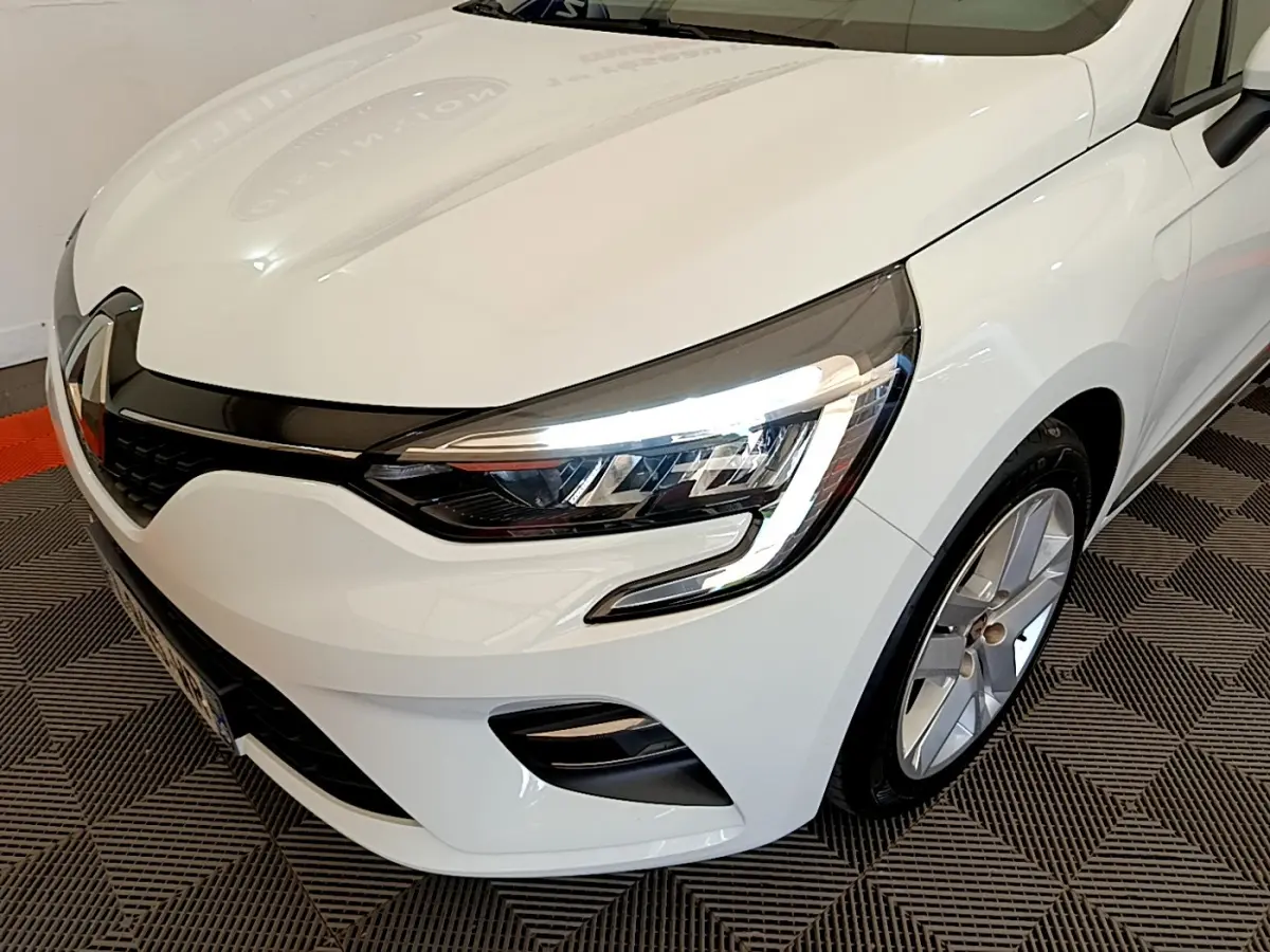 Vue 3/4 avant droit d'une Renault Clio Business blanche mettant en valeur ses phares LED et sa calandre noire brillante.