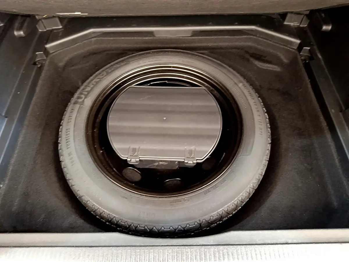 Vue plongeante sur la roue de secours et le rangement sous tablette dans le coffre du Peugeot 3008 gris foncé.