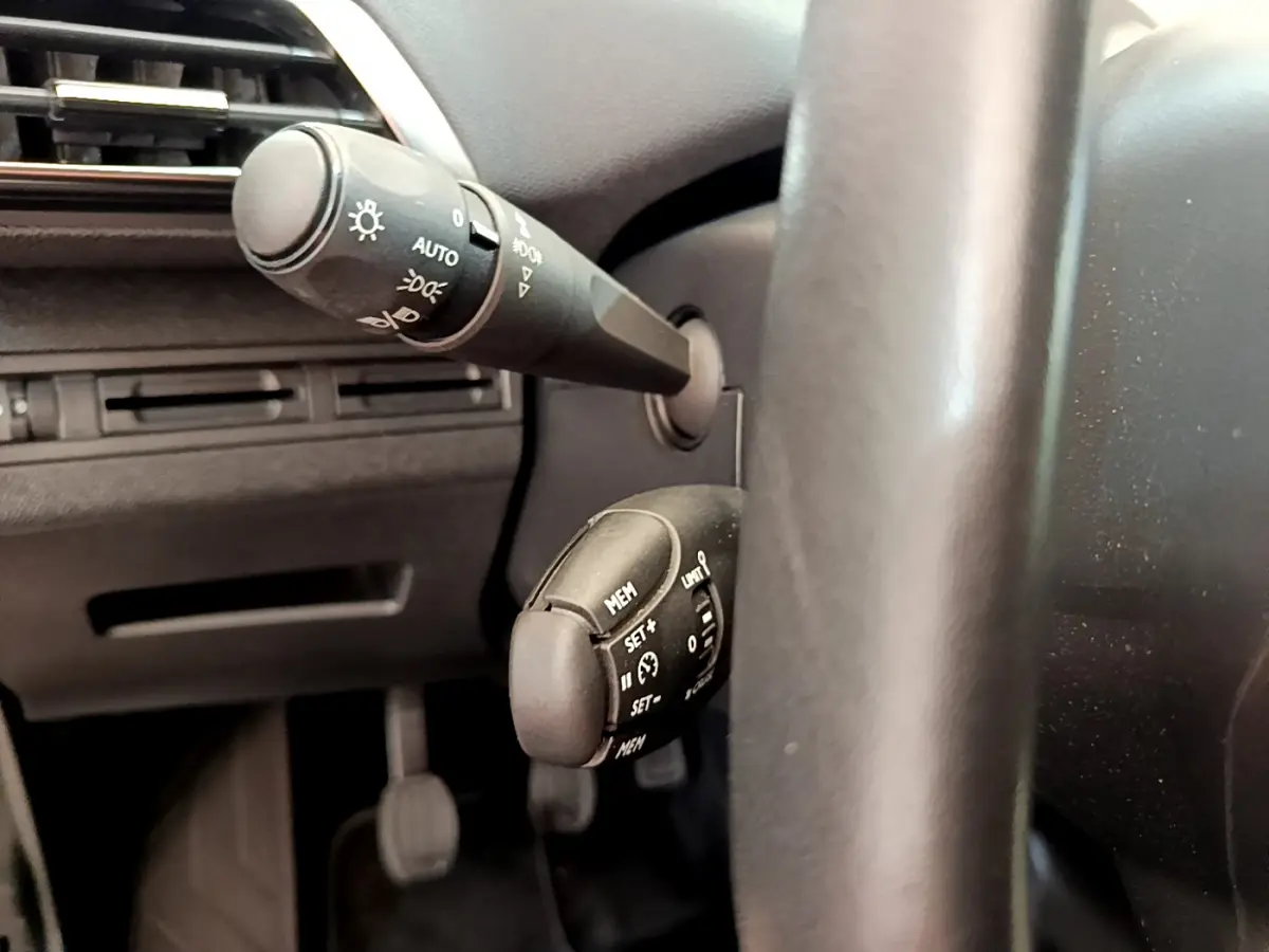 Gros plan sur les commandes de régulateur de vitesse et éclairage à gauche du volant cuir du Peugeot 3008 gris foncé 2020.