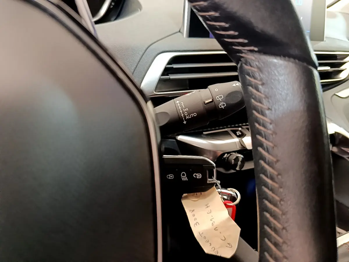 Gros plan intérieur sur le volant cuir et la commande des essuie-glaces d’un Peugeot 3008 gris foncé, version Puretech 130 S&S ACTIVE.