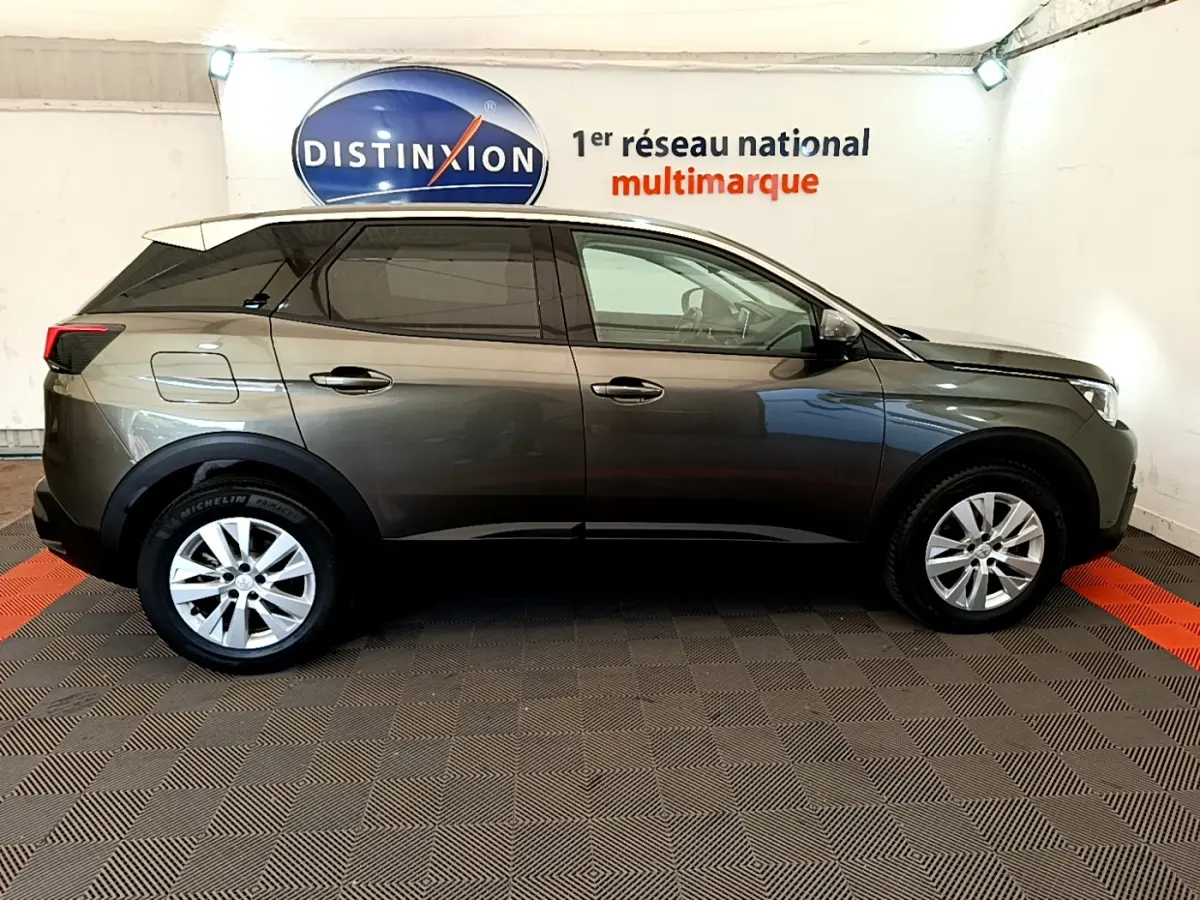 Vue de profil côté gauche d'un Peugeot 3008 gris foncé, stationné en intérieur sur sol à damiers noirs et rouges.