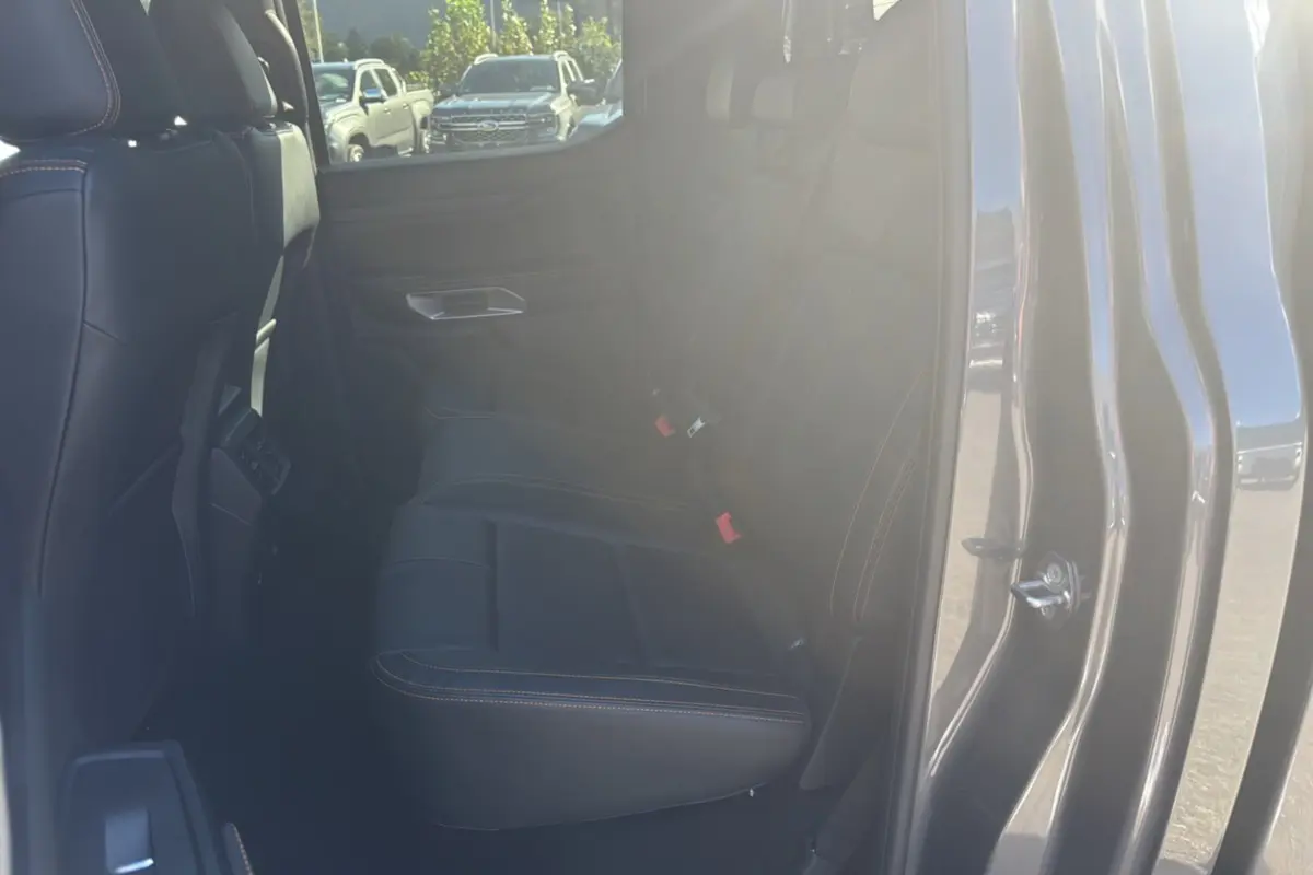 Vue intérieure côté droit du Ford Ranger Wildtrak 2025 gris carbone, montrant les sièges arrière en cuir noir avec surpiqûres orange.