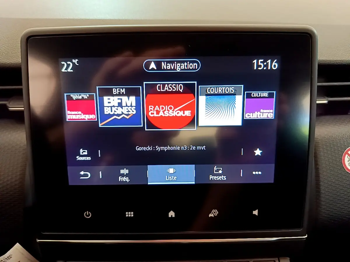 Écran tactile central allumé de la Renault Clio Business blanche, affichant les stations radio et la navigation.