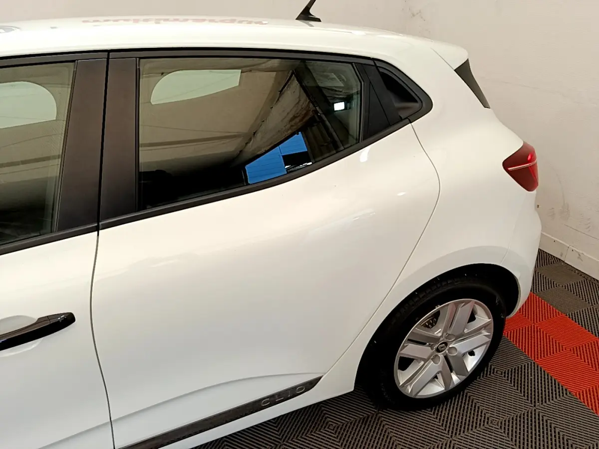 Vue latérale arrière droite d'une Renault Clio blanche avec jante alliage et logo Clio sur la porte arrière.