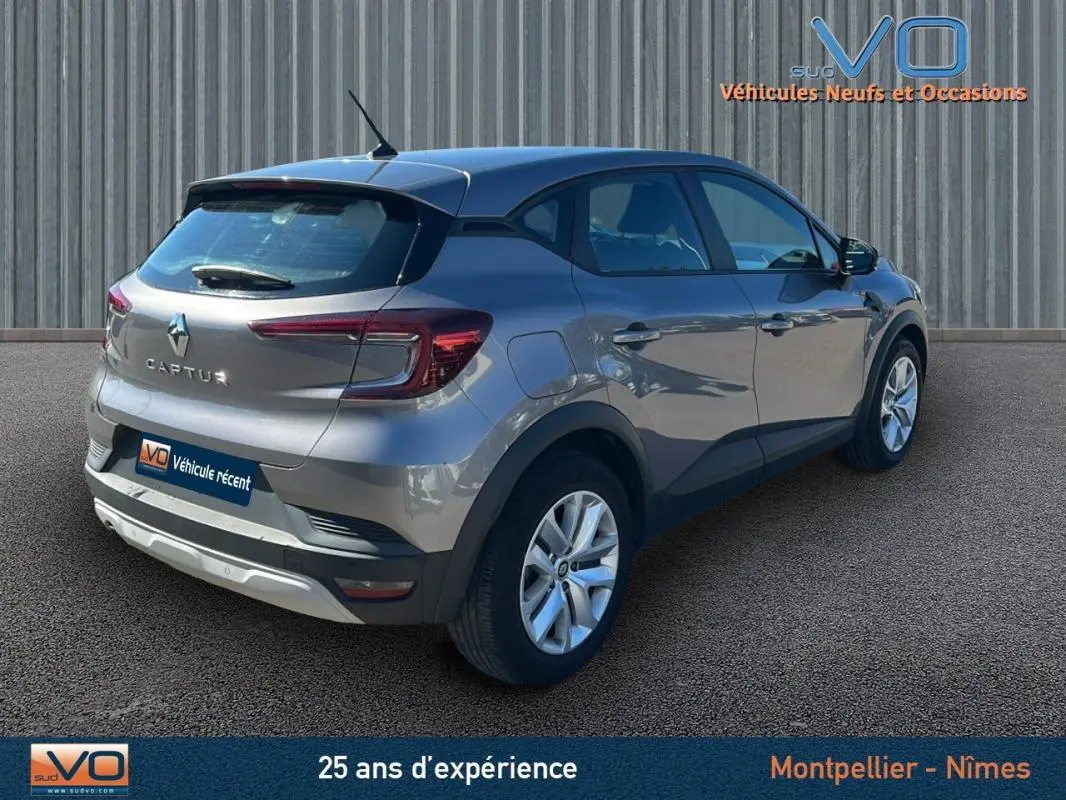 Vue 3/4 arrière droite d'un Renault Captur gris 2021 garé devant un mur métallique.