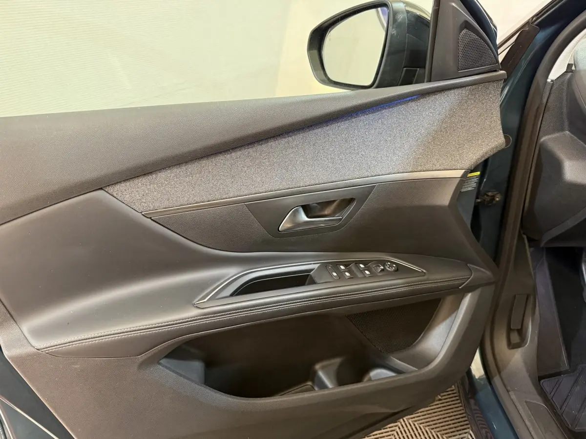 Vue intérieure côté gauche de la porte avant d’un Peugeot 5008 bleu, avec commandes électriques et garniture noire.