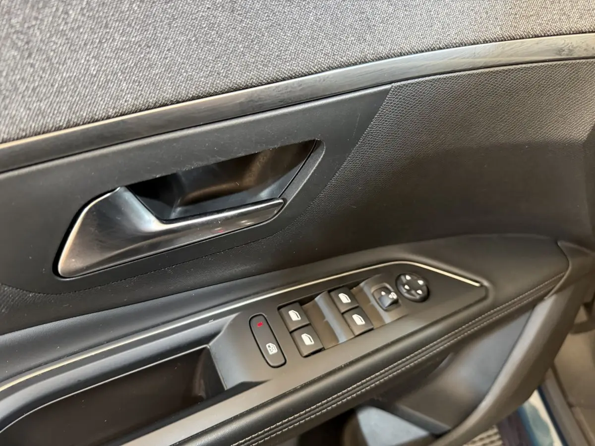 Gros plan sur la porte côté conducteur du Peugeot 5008 bleu, montrant les commandes électriques des vitres et le bouton de verrouillage.