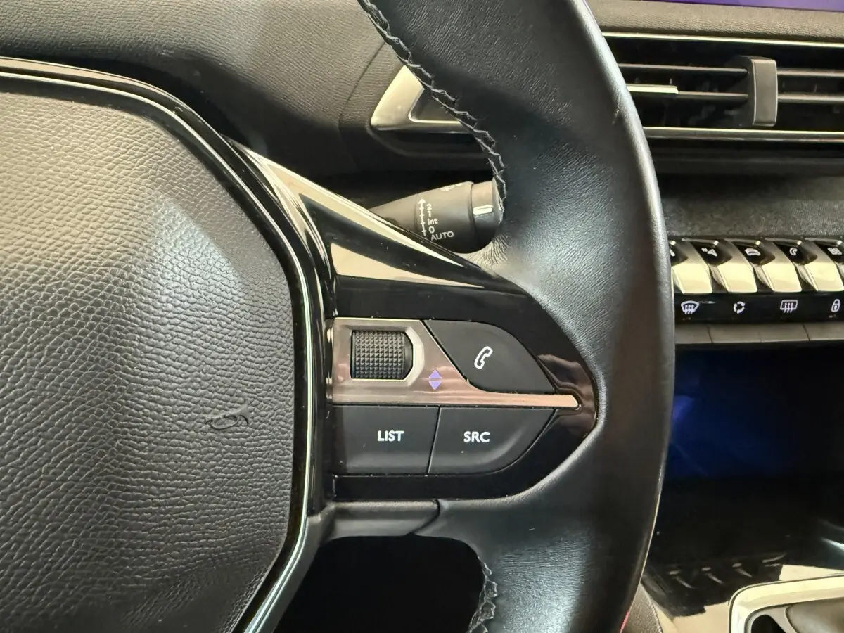 Gros plan sur le volant cuir multifonctions noir côté gauche du Peugeot 5008 bleu, avec commandes audio et téléphone.